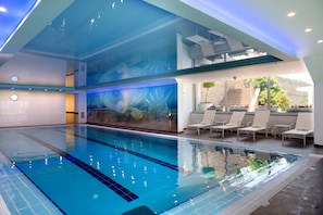 Une piscine intérieure moderne avec de l’eau d’un bleu cristallin, une fresque représentant la vie aquatique et un espace détente avec des chaises longues.