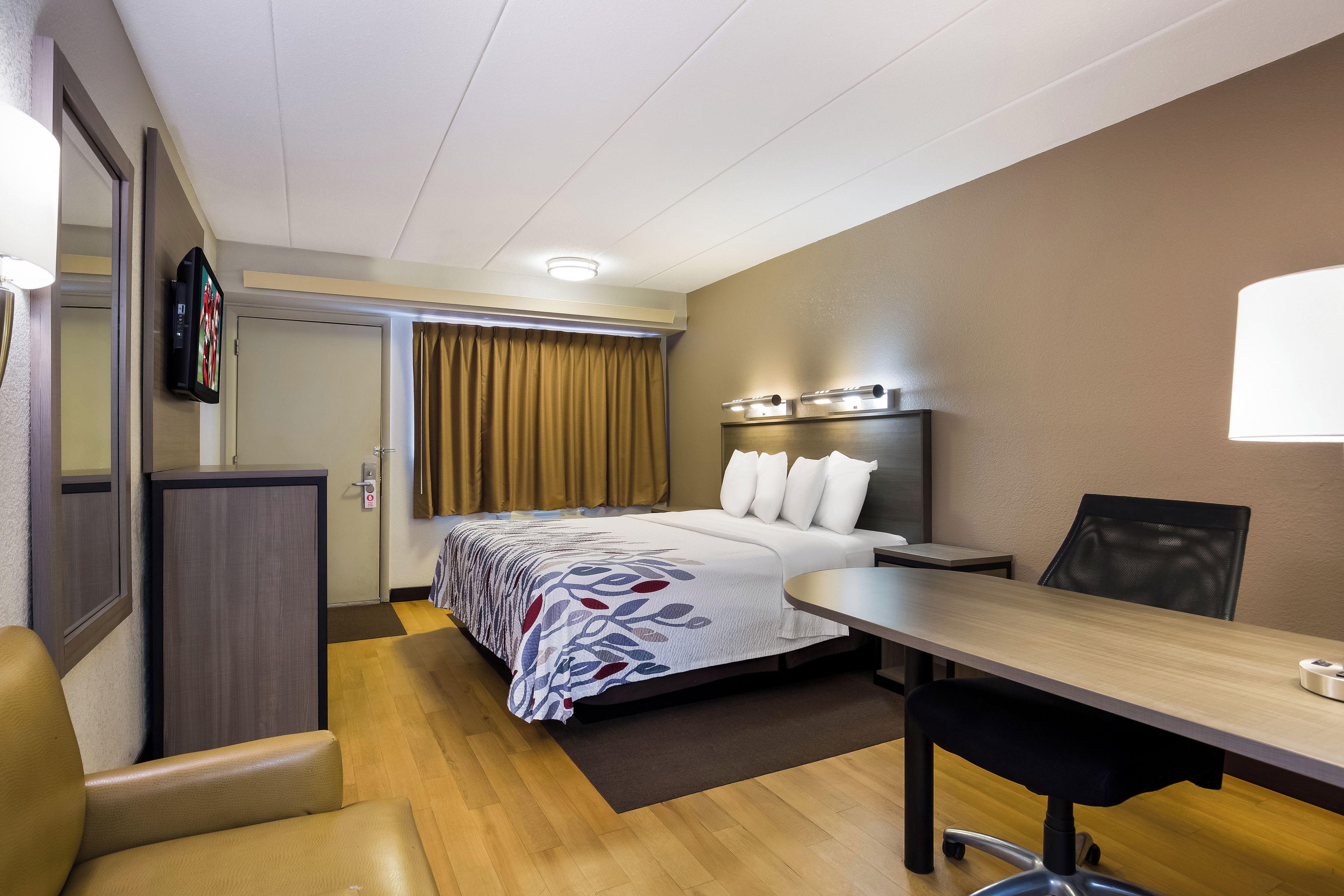 Una habitación de hotel con cama, escritorio, silla y televisor.