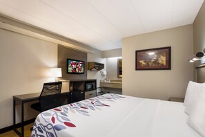 Una habitación de hotel con cama, escritorio, silla, televisor y microondas.