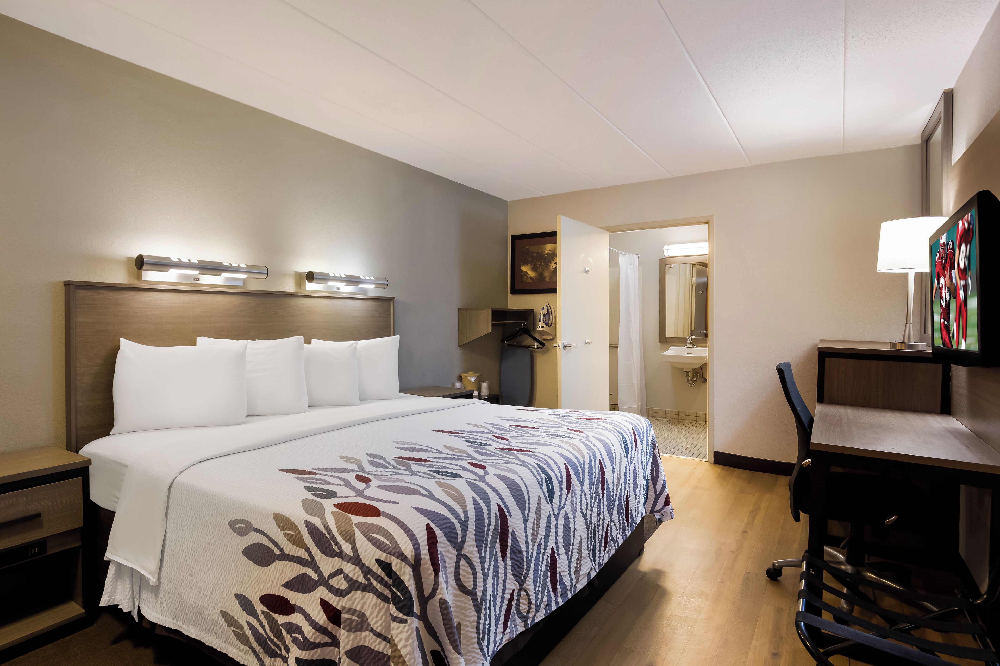 A hotel room with a large bed, a desk with a chair, a bathroom with a sink, and a TV.
