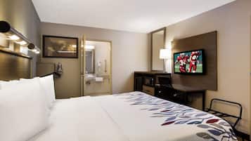 Quarto de hotel com cama, escrivaninha, televisão e banheiro visível por uma porta aberta.