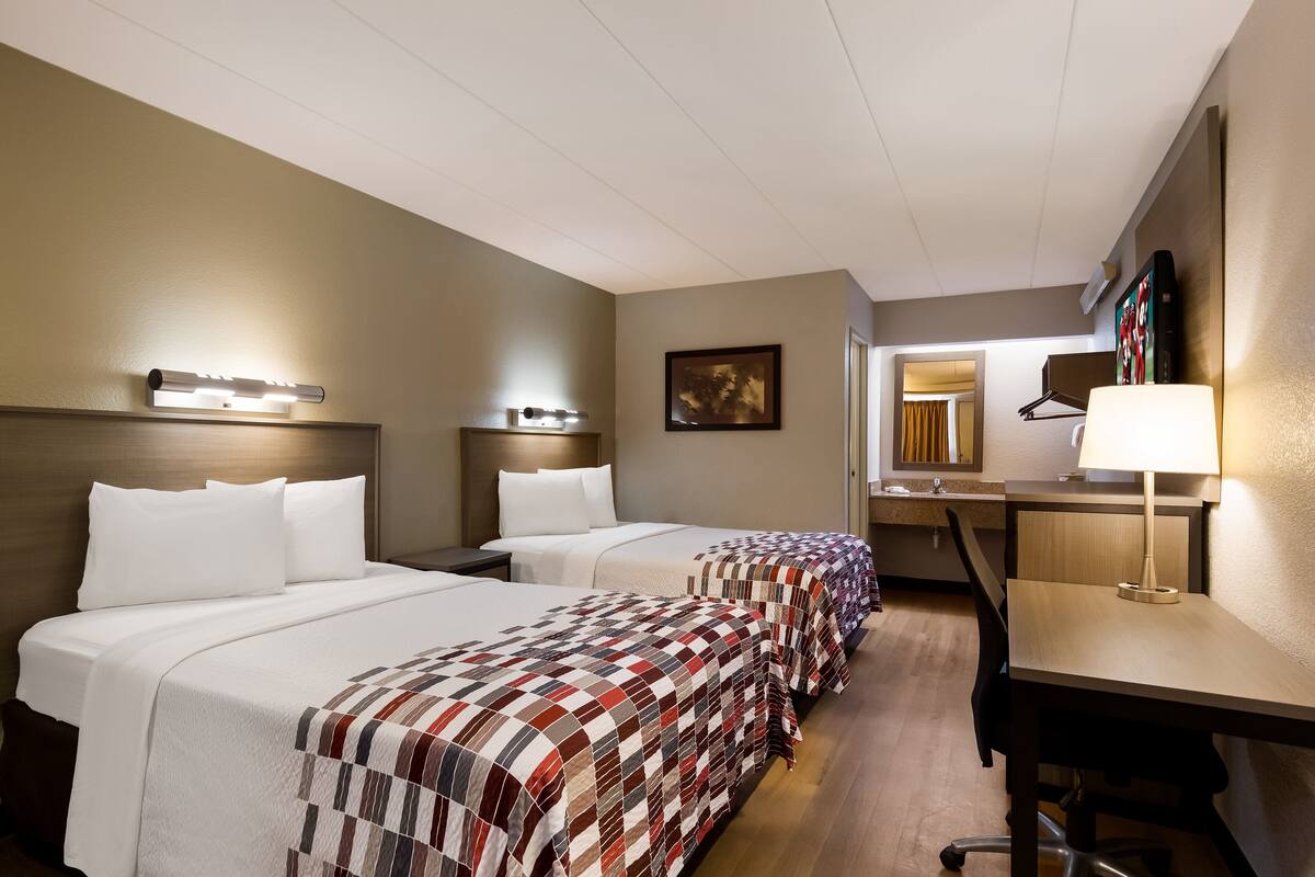 A hotel room with two beds, a desk, and a chair.