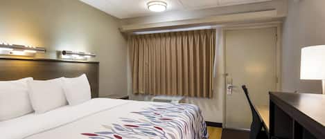 Una habitación de hotel con una cama, un escritorio, una lámpara, una ventana con cortinas y una puerta.