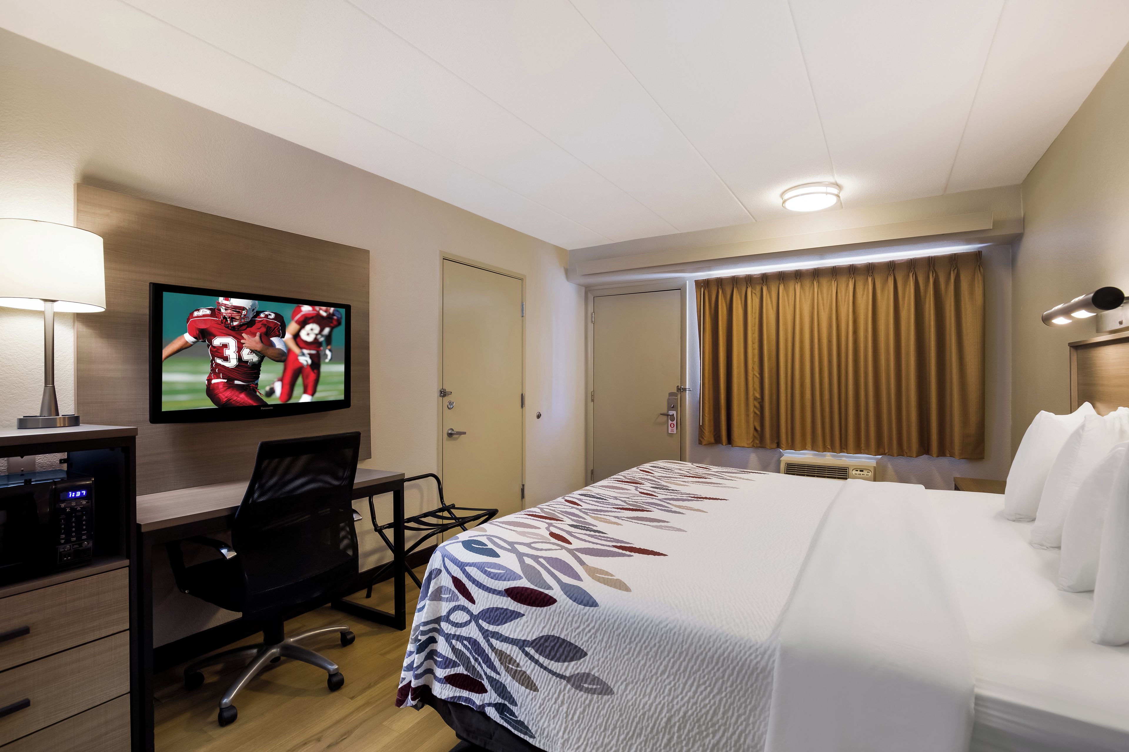 A hotel room with a bed, a desk with a computer, a television, and a door.
