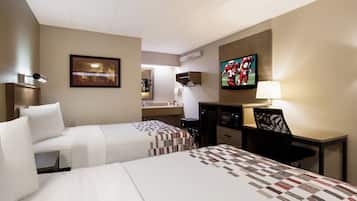 A hotel room with two beds, a desk, a television, and a bathroom visible through an open door.