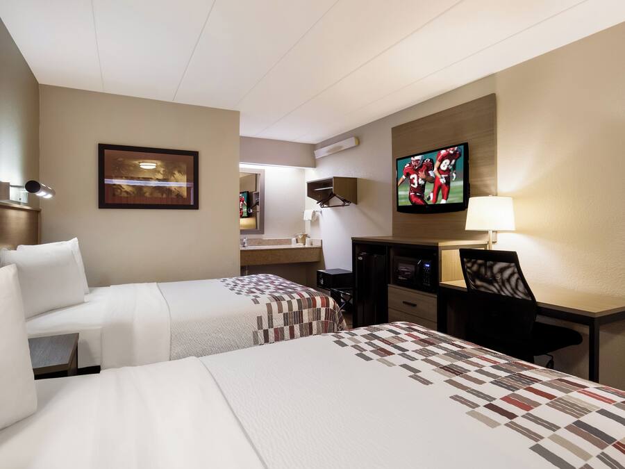 Ein Hotelzimmer mit zwei Betten, einem Schreibtisch, einem Fernseher und einem durchgegangenen Badezimmer.