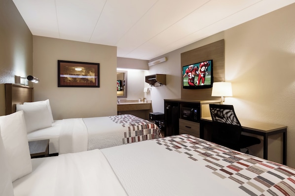 Une chambre d’hôtel avec deux lits, un bureau, une télévision et une salle de bain visible à travers une porte ouverte.