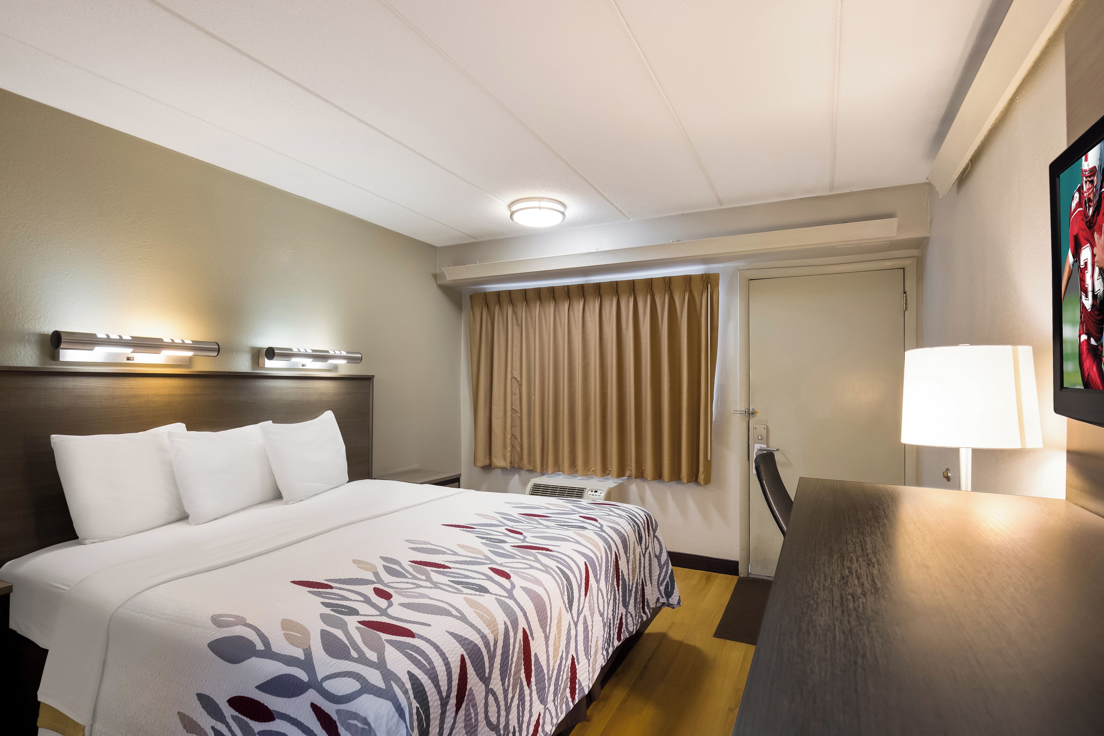 Hotellihuone, jossa on sänky, yöpöytä, lamppu ja ikkunasta avautuva näkymä ulos.