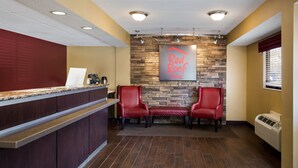 Zona de recepción con pared de piedra, dos sillones rojos, un mostrador de recepción y un cartel en la pared.