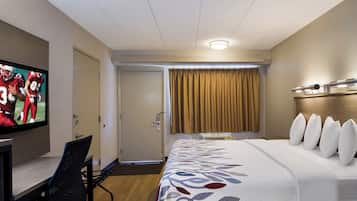 A hotel room with a bed, a TV, a desk, and a window with curtains.