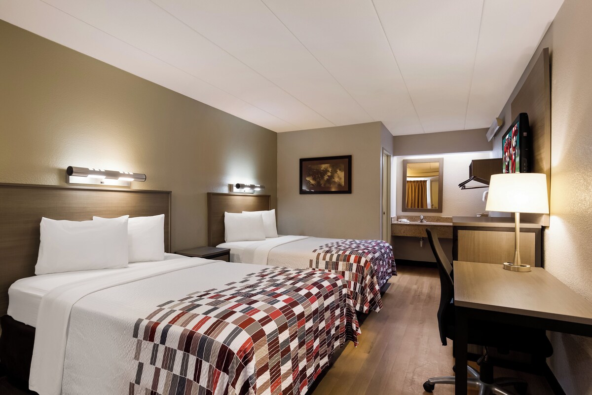 A hotel room with two beds, a desk, and a chair.