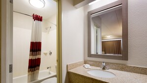 Un baño con una bañera blanca, un inodoro blanco, un lavabo con encimera de granito y un espejo sobre el lavabo.