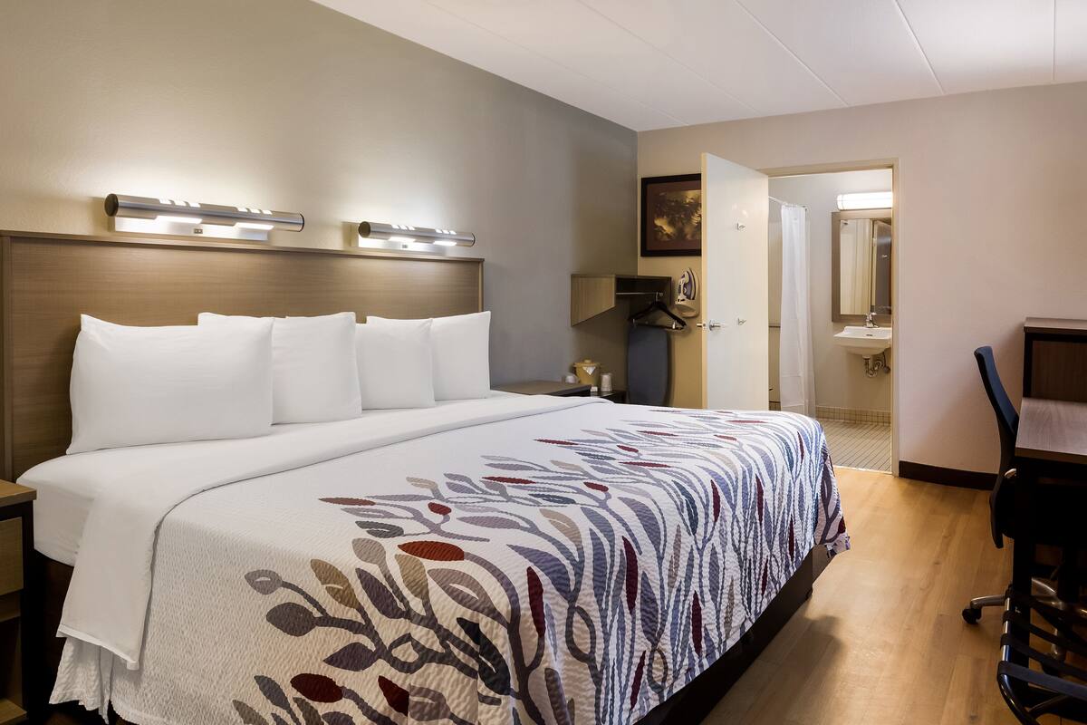 A hotel room with a large bed, bedside tables, a desk, and a bathroom visible through an open door.