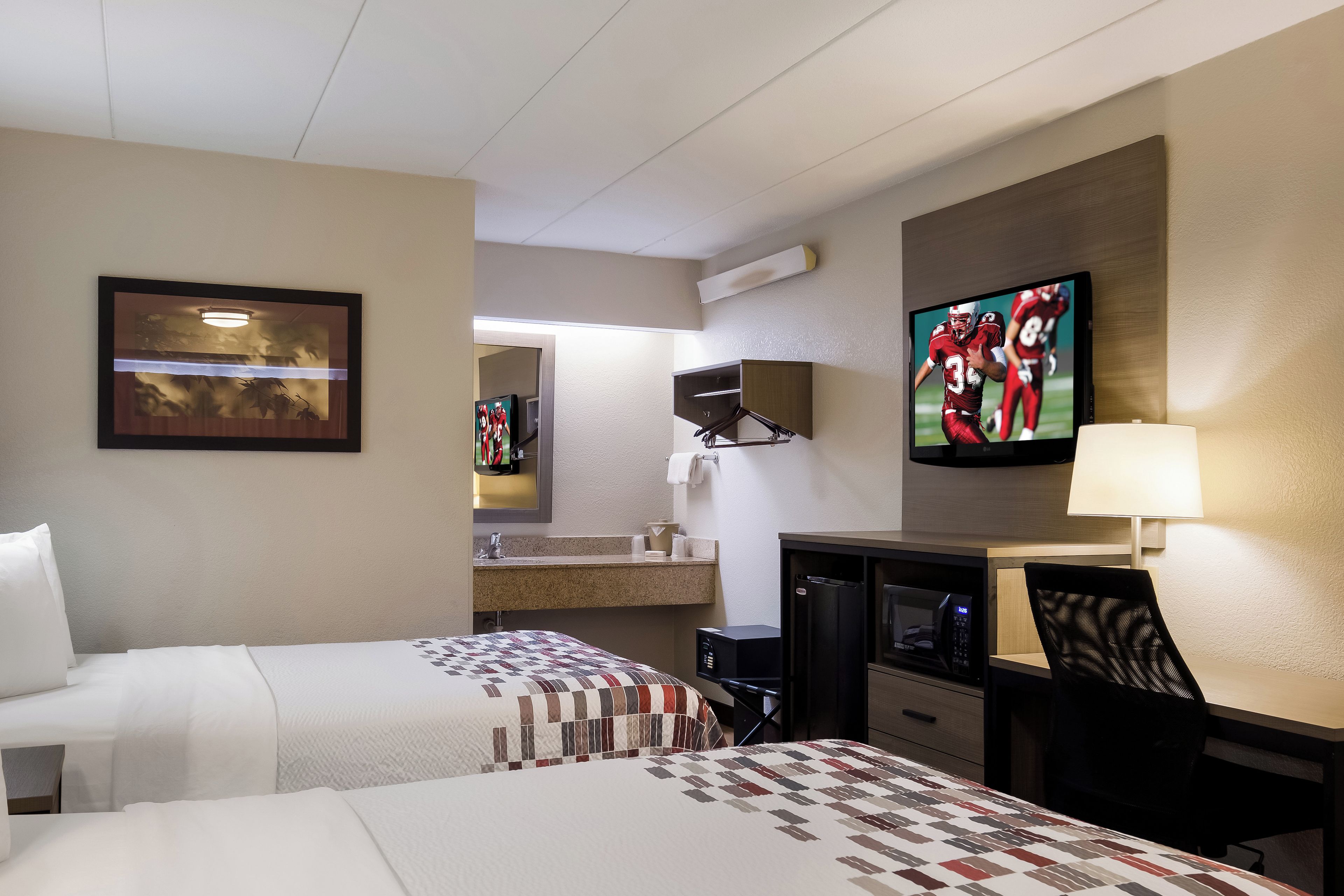 A hotel room with two beds, a desk, a television, a mirror, and a window.