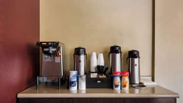 Una estación de café con máquina de café, vasos desechables y dispensadores de leche para café.