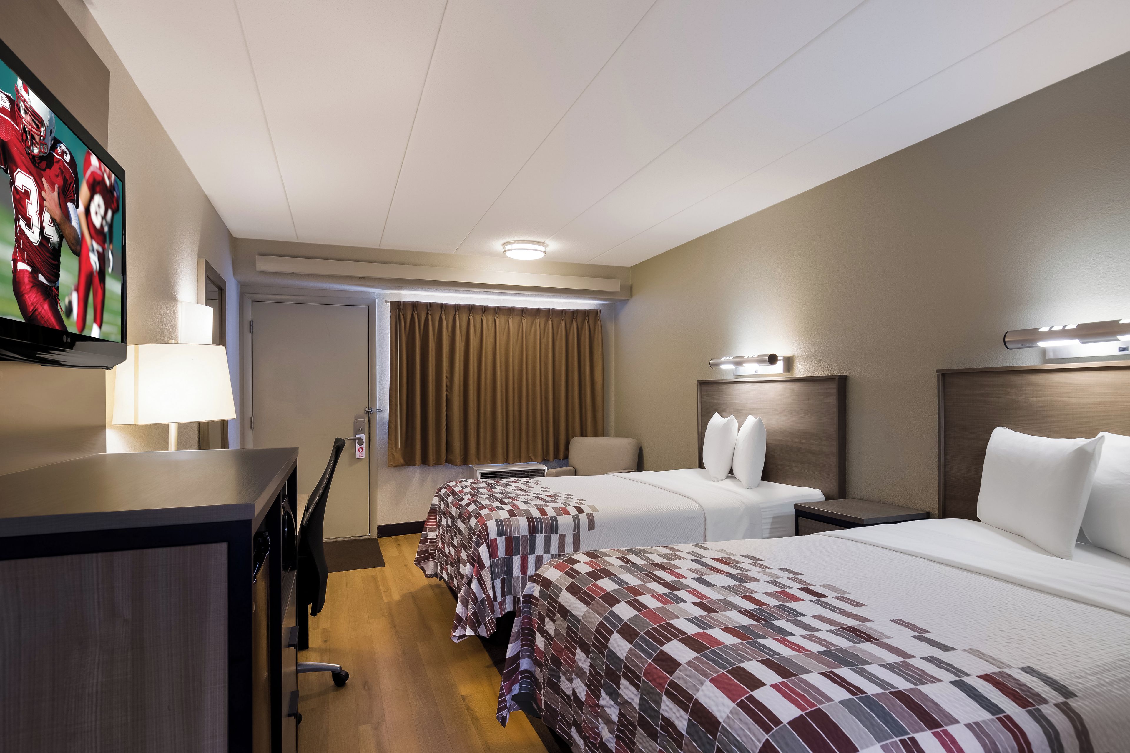 A hotel room with two beds, a desk, a chair, a television, and a door.