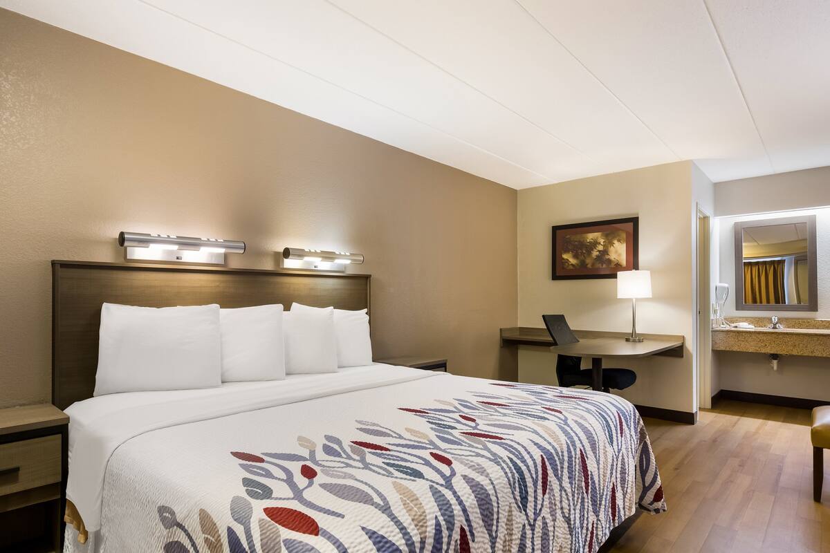 A hotel room with a large bed, a desk, a chair, and a bathroom mirror.
