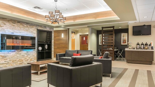 Una hall d'hotel moderna con un caminetto, posti a sedere confortevoli, una reception e un televisore.