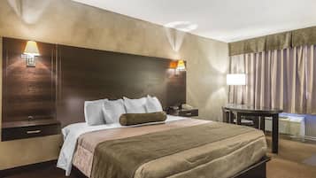 A hotel room with a large bed, bedside lamps, a desk, and a window with curtains.