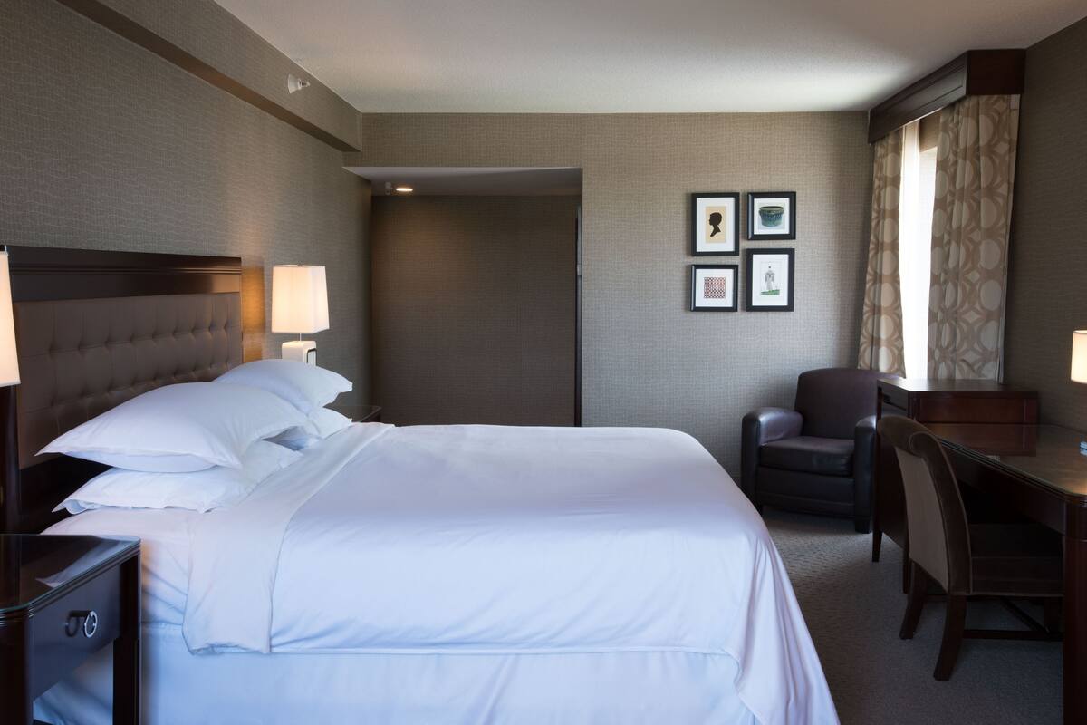 A hotel room with a large bed, a desk, a chair, and framed pictures on the wall.