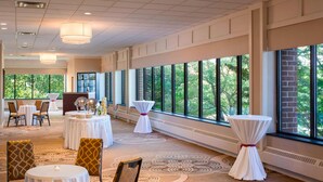 A spacious hotel lobby with large windows, round tables, and patterned carpet. - Sheraton Harrisburg Hershey Hotel (Harrisburg)