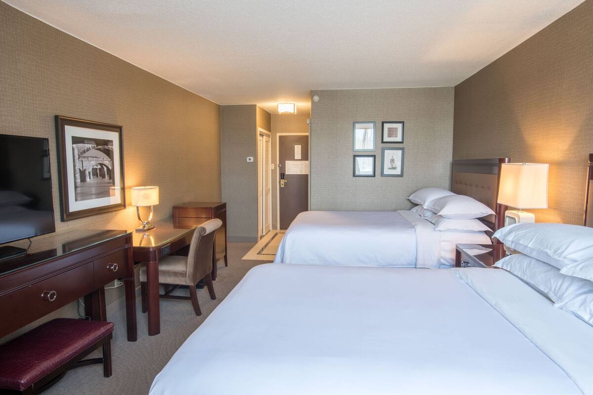 A hotel room with two beds, a desk, a chair, and a television.