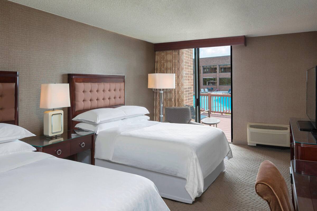 A hotel room with two beds, a desk, a chair, and a view of a pool.