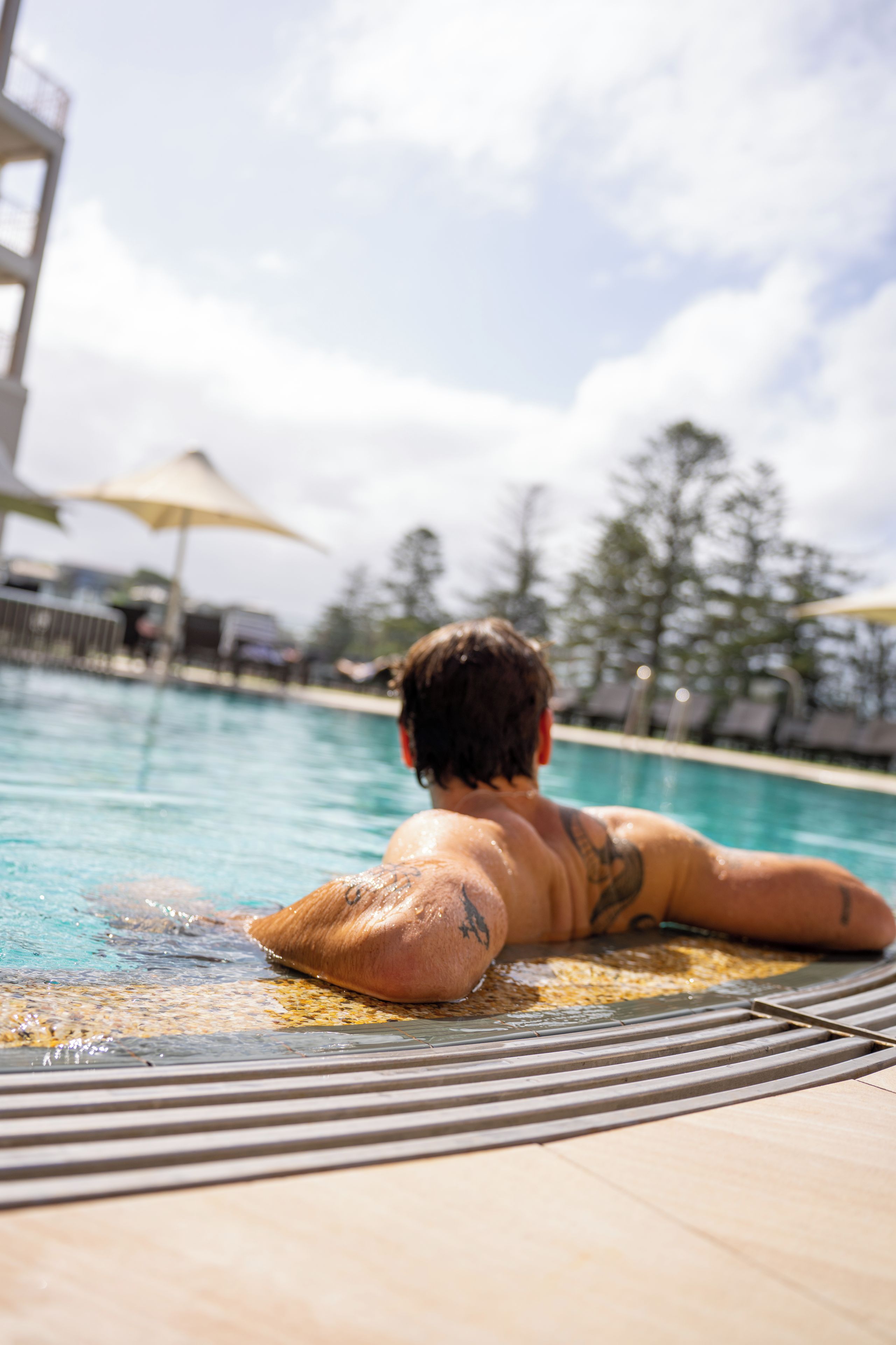 Une personne se détend dans une piscine, avec un ciel dégagé et des arbres en arrière-plan.