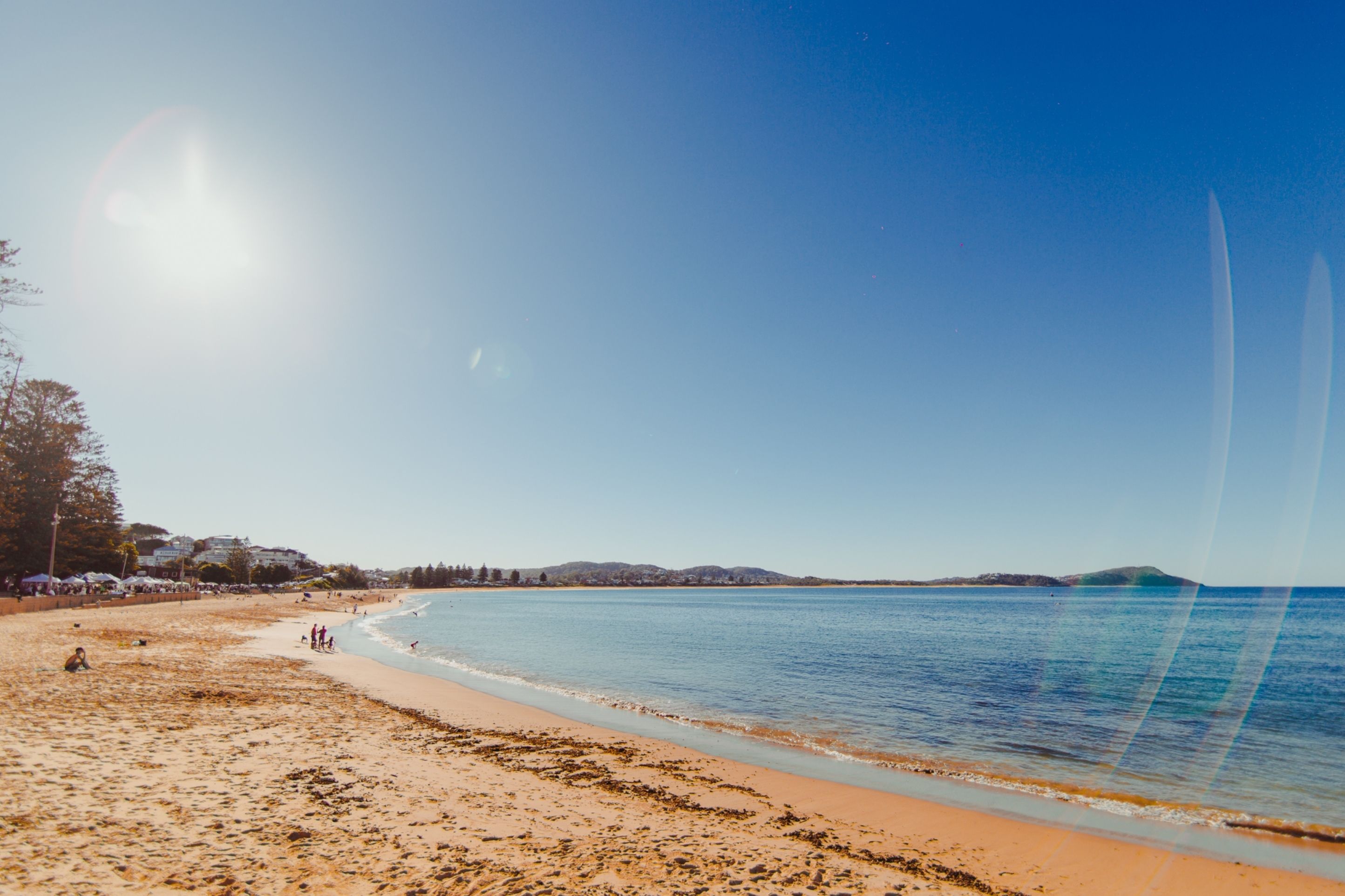A beach with clear skies, calm water, and distant hills.