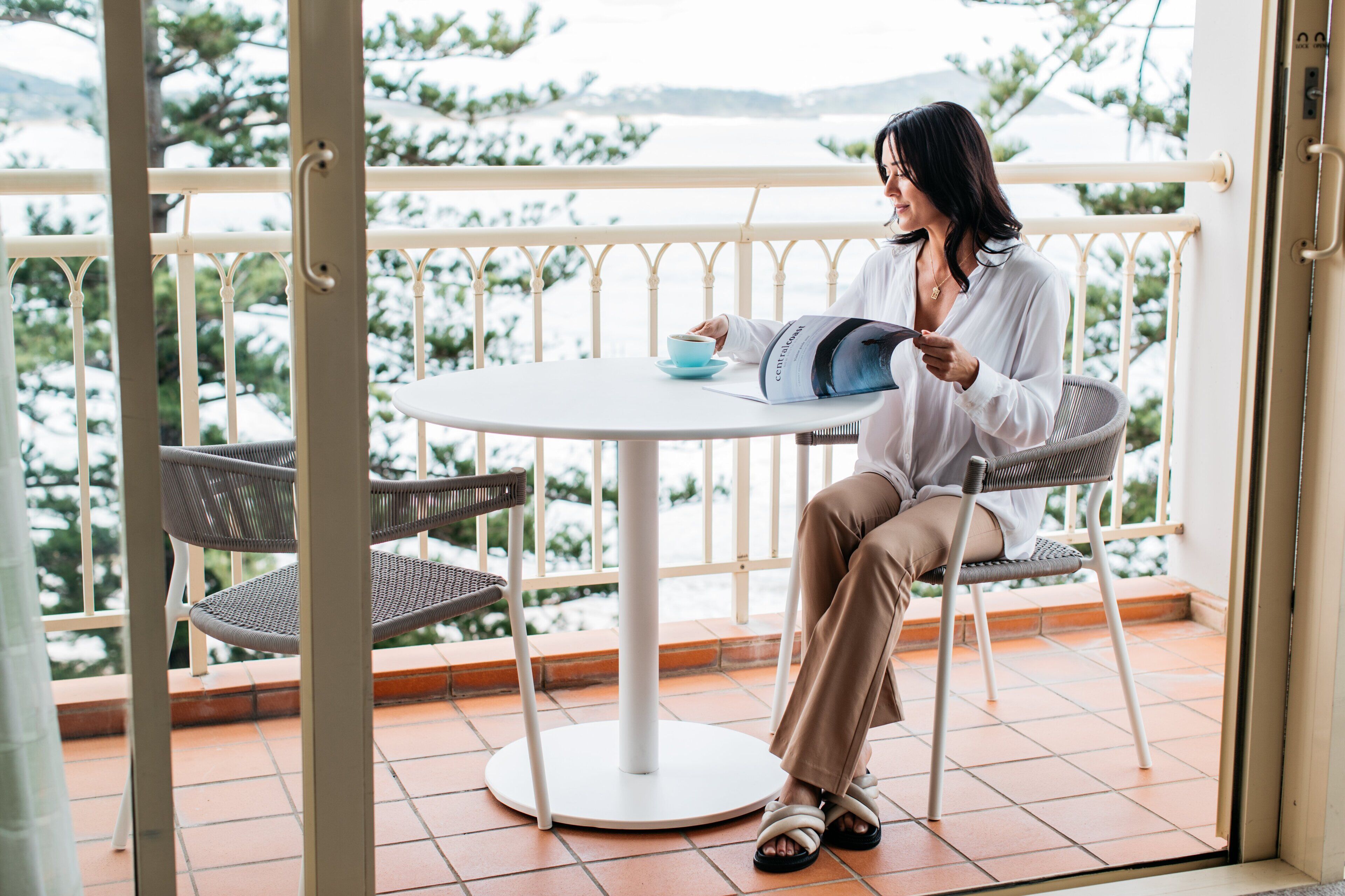 A person sitting at a round table with a chair, holding a magazine.