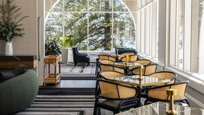 A modern dining area with a glass table and wicker chairs, large windows with a view of trees, and a green sofa. - Crowne Plaza Terrigal Pacific by IHG (Terrigal)