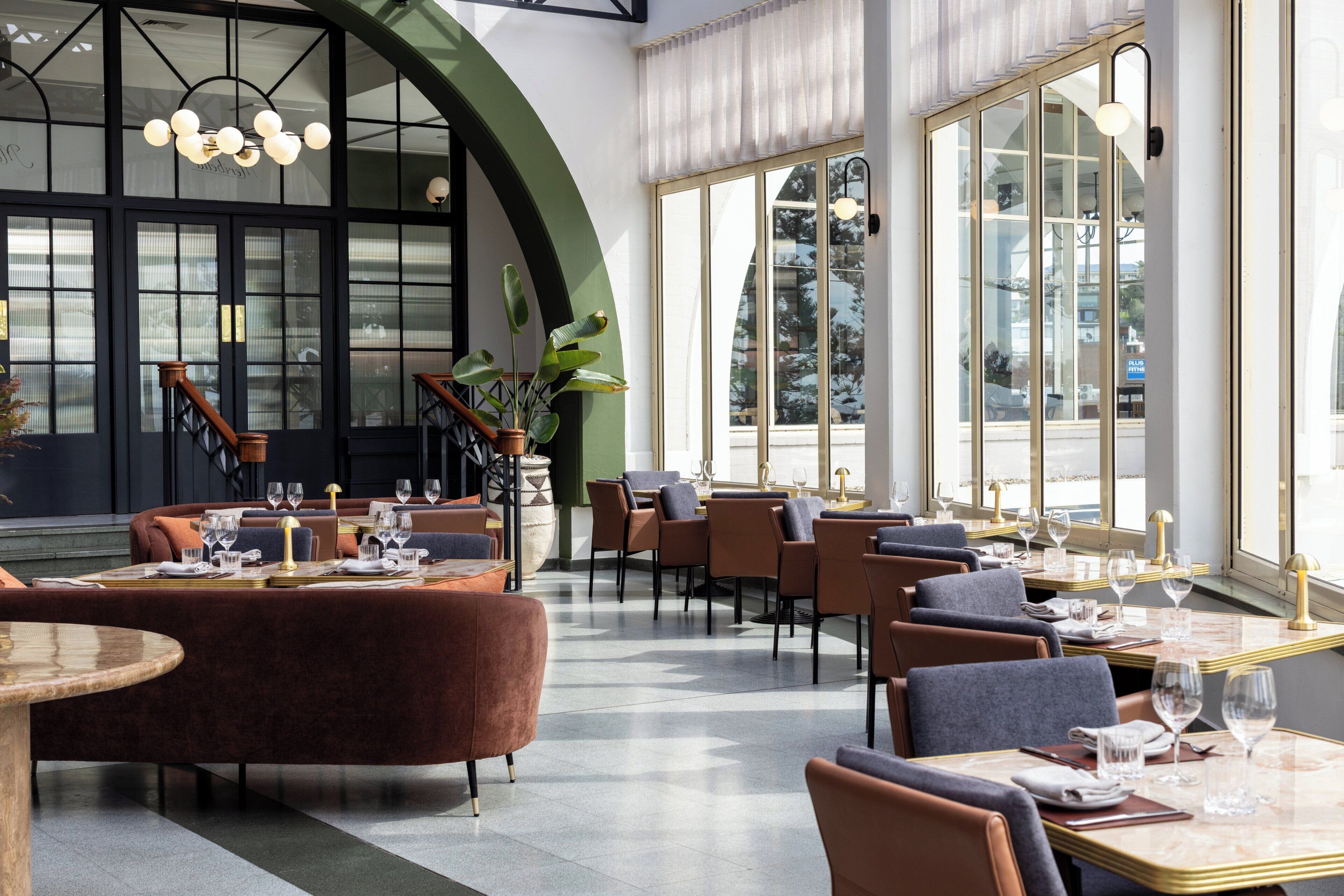 A restaurant interior with high ceilings, large windows, and a mix of seating arrangements including tables and booths.