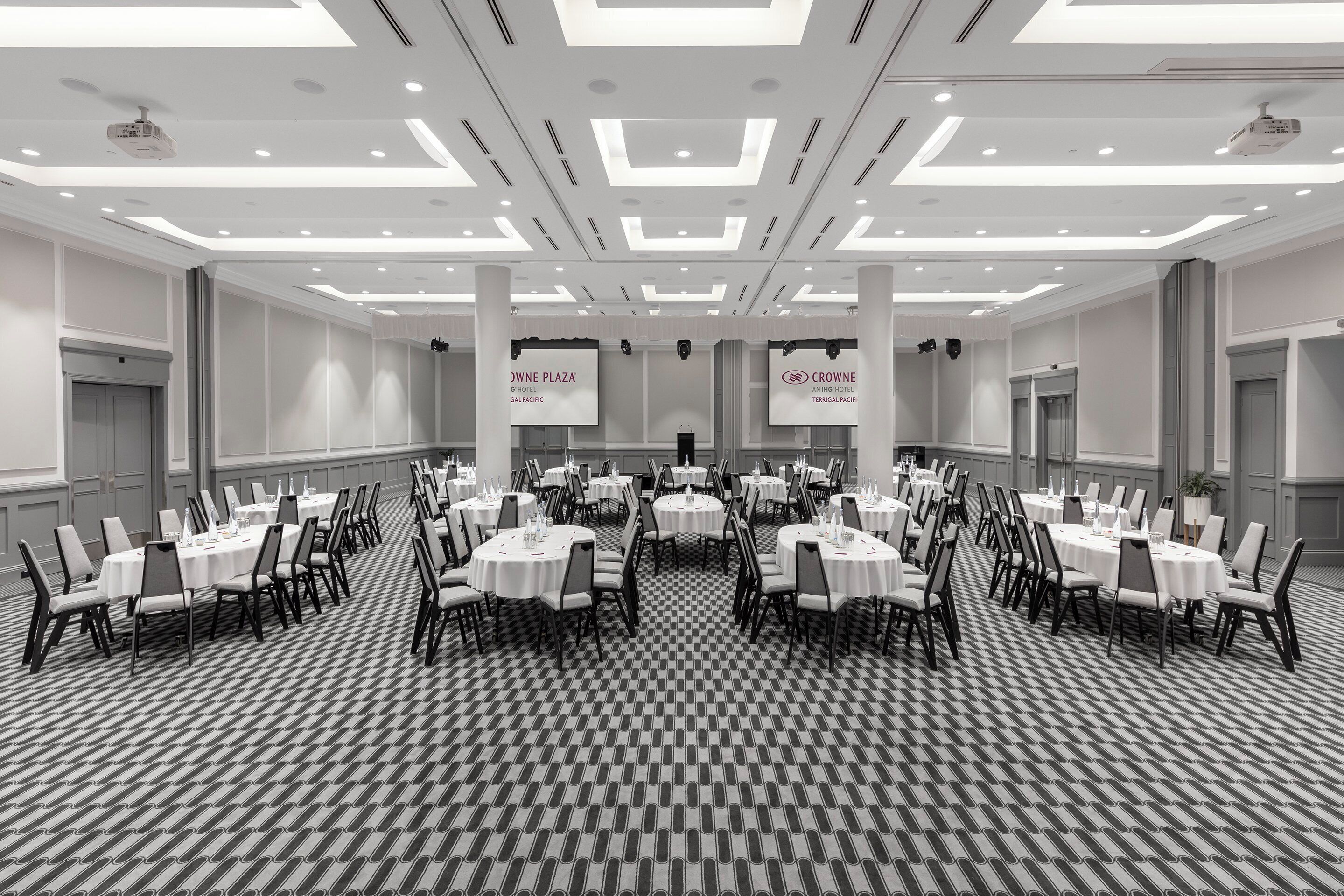 A large conference room with multiple round tables and chairs, arranged in rows.