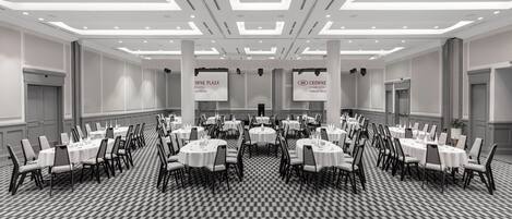 A large conference room with multiple round tables and chairs, arranged in rows.