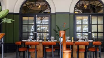 A dining area with a round table set for six, surrounded by orange upholstered chairs.