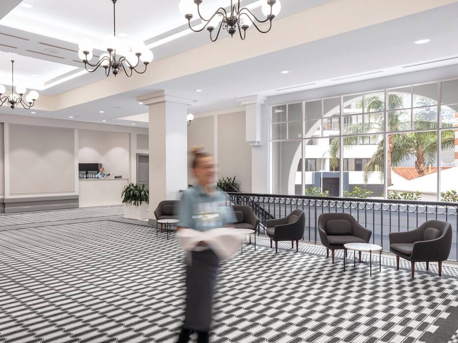 Een ruime lobby met een patroon vloer, moderne meubels en grote ramen met uitzicht op de omgeving.