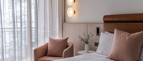 A hotel room with a bed, a chair, a small table with a vase, and two wall-mounted lights.