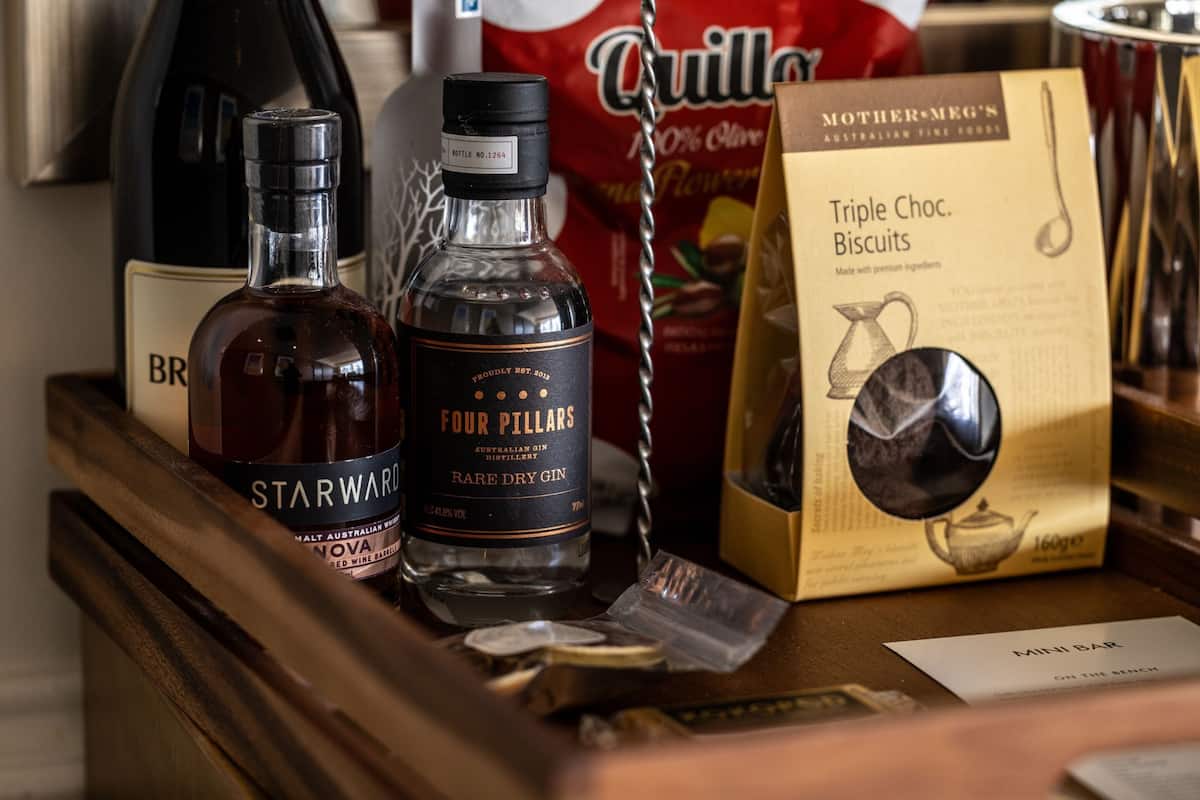 Una zona de bar con botellas de ginebra Starward y Four Pillars, una caja de galletas de chocolate de Quill y un cartel de 'Mini Bar'.
