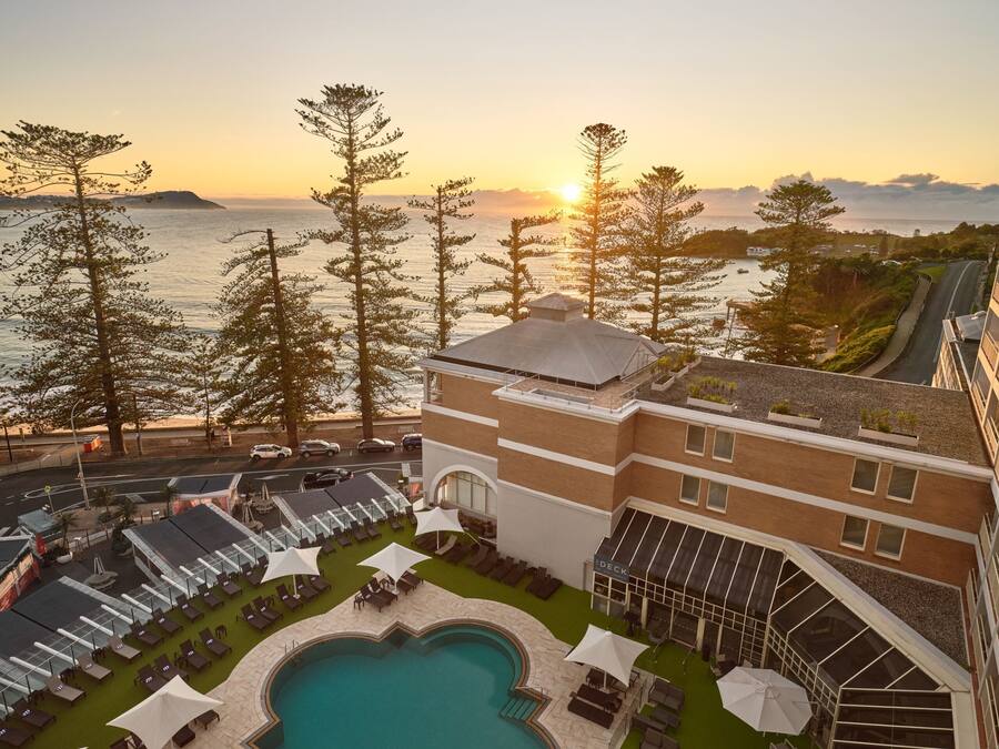 Un hotel con zona de piscina, mobiliario exterior y vistas al mar al atardecer.