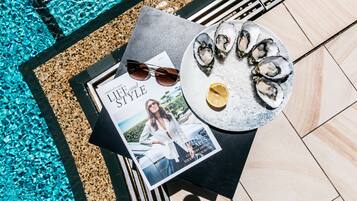 A table with a magazine, sunglasses, a plate of oysters, and a lemon wedge.