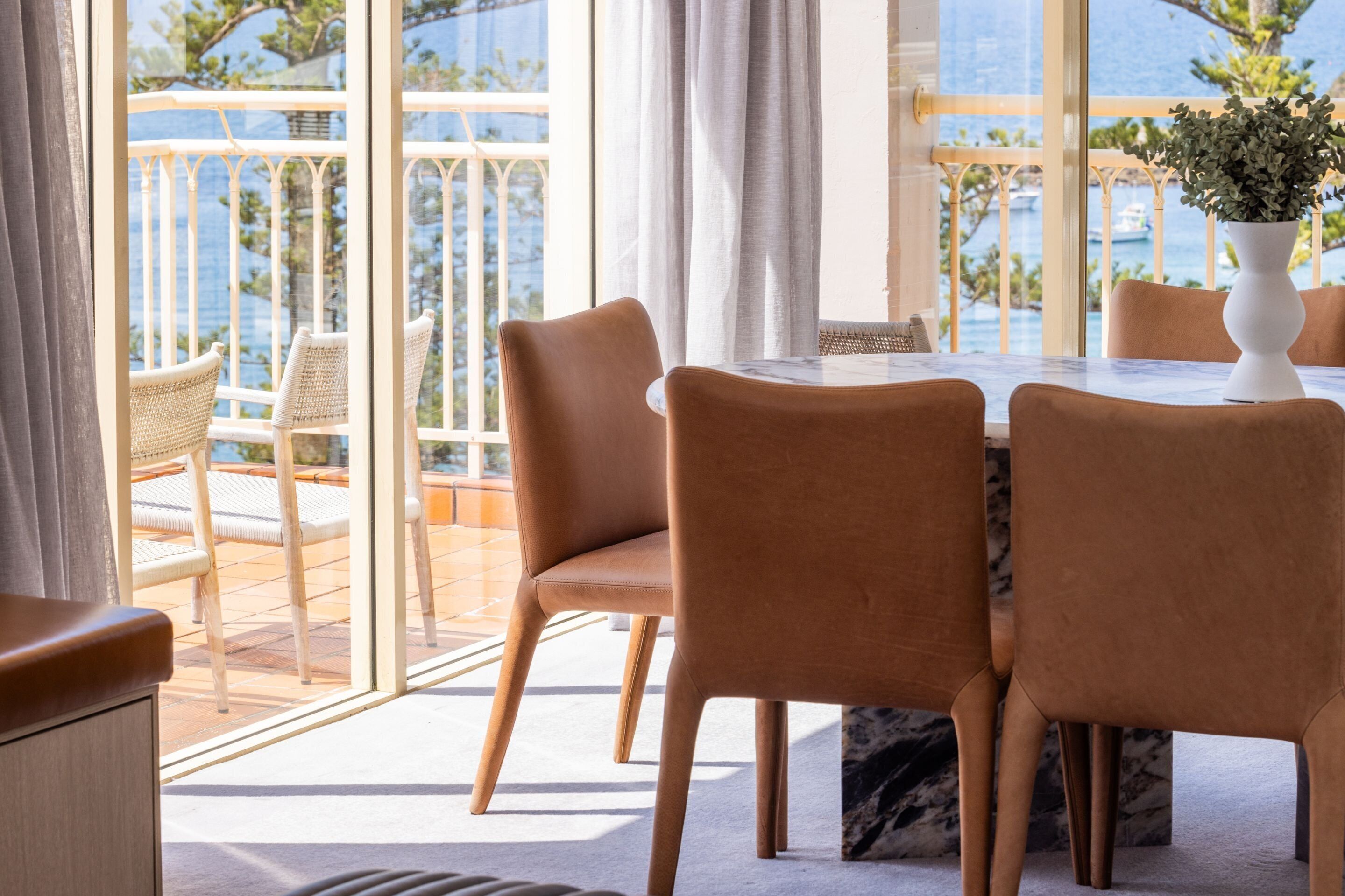 Un coin repas avec une table et des chaises, de grandes fenêtres donnant sur la mer et une plante en pot posée sur la table.
