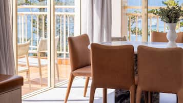 Un coin repas avec une table et des chaises, de grandes fenêtres donnant sur la mer et une plante en pot posée sur la table.