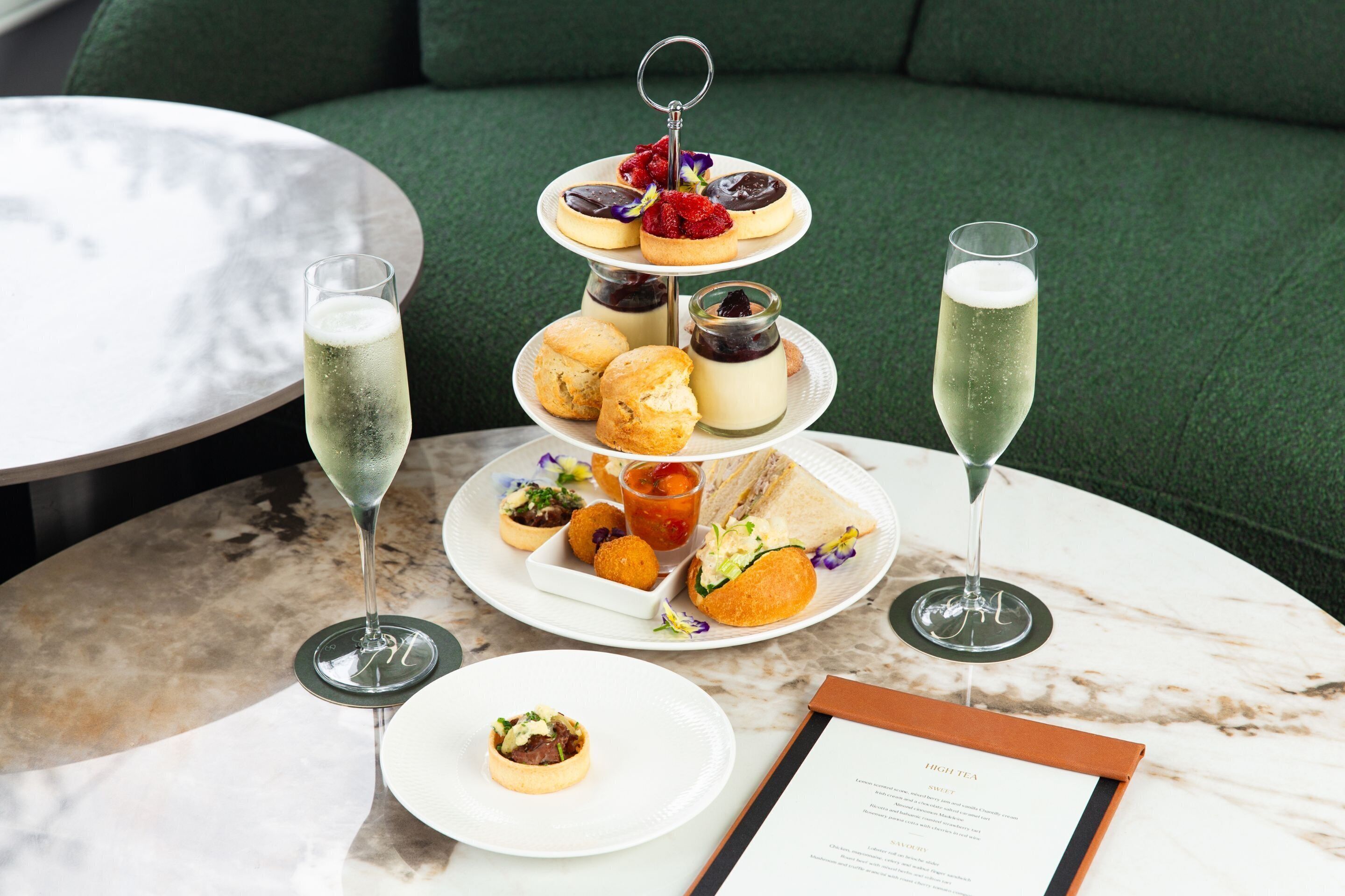 Un présentoir à trois niveaux, garni de diverses pâtisseries, et une coupe de champagne posée sur une table en marbre.