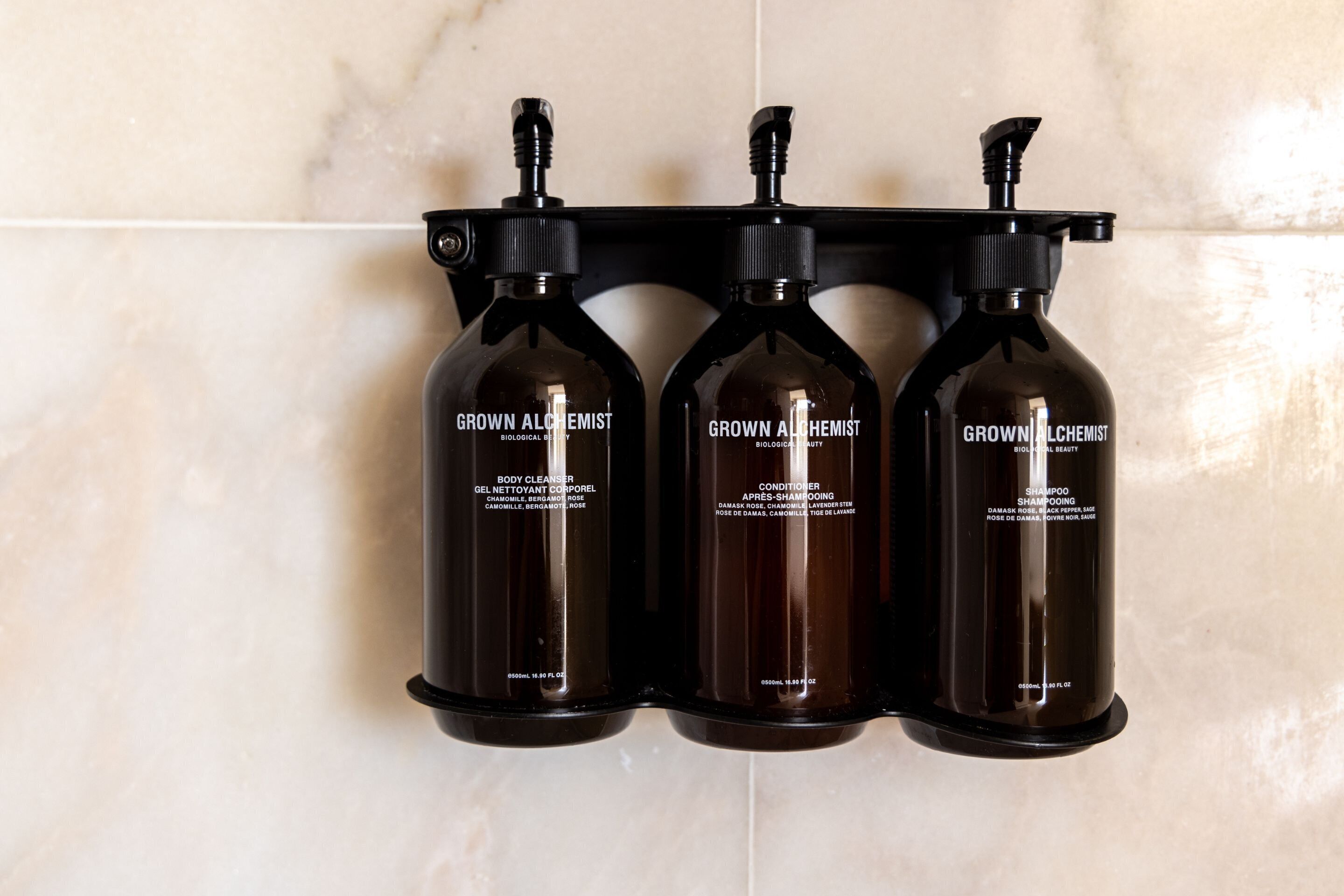 Trois bouteilles de produits de la marque « Grown Alchemist » sont disposées sur un support noir fixé au mur.