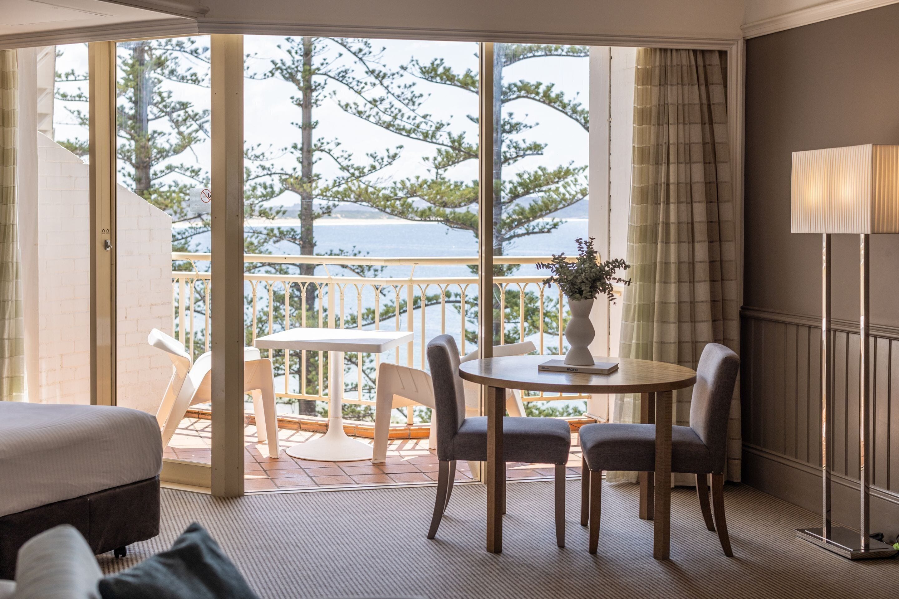 A hotel room with a balcony, a dining table with chairs, a lamp, and a bed.