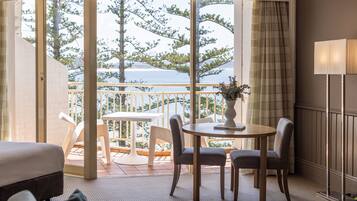 A hotel room with a balcony, a dining table with chairs, a lamp, and a bed.
