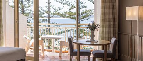 Une chambre d’hôtel avec un balcon, une table à manger avec des chaises, une lampe et un lit.
