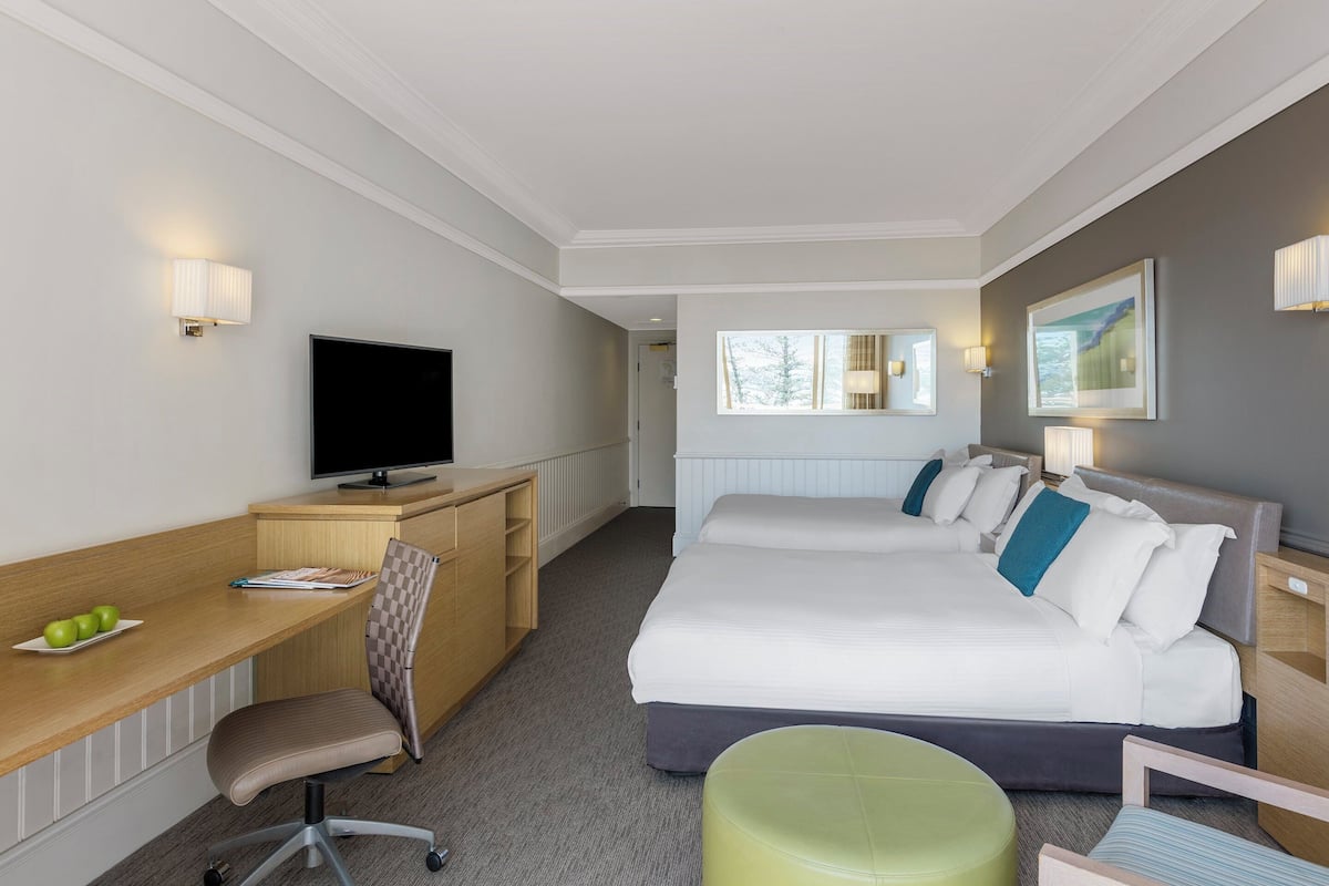 Una habitación de hotel con cama, escritorio, silla, televisor y ventana.