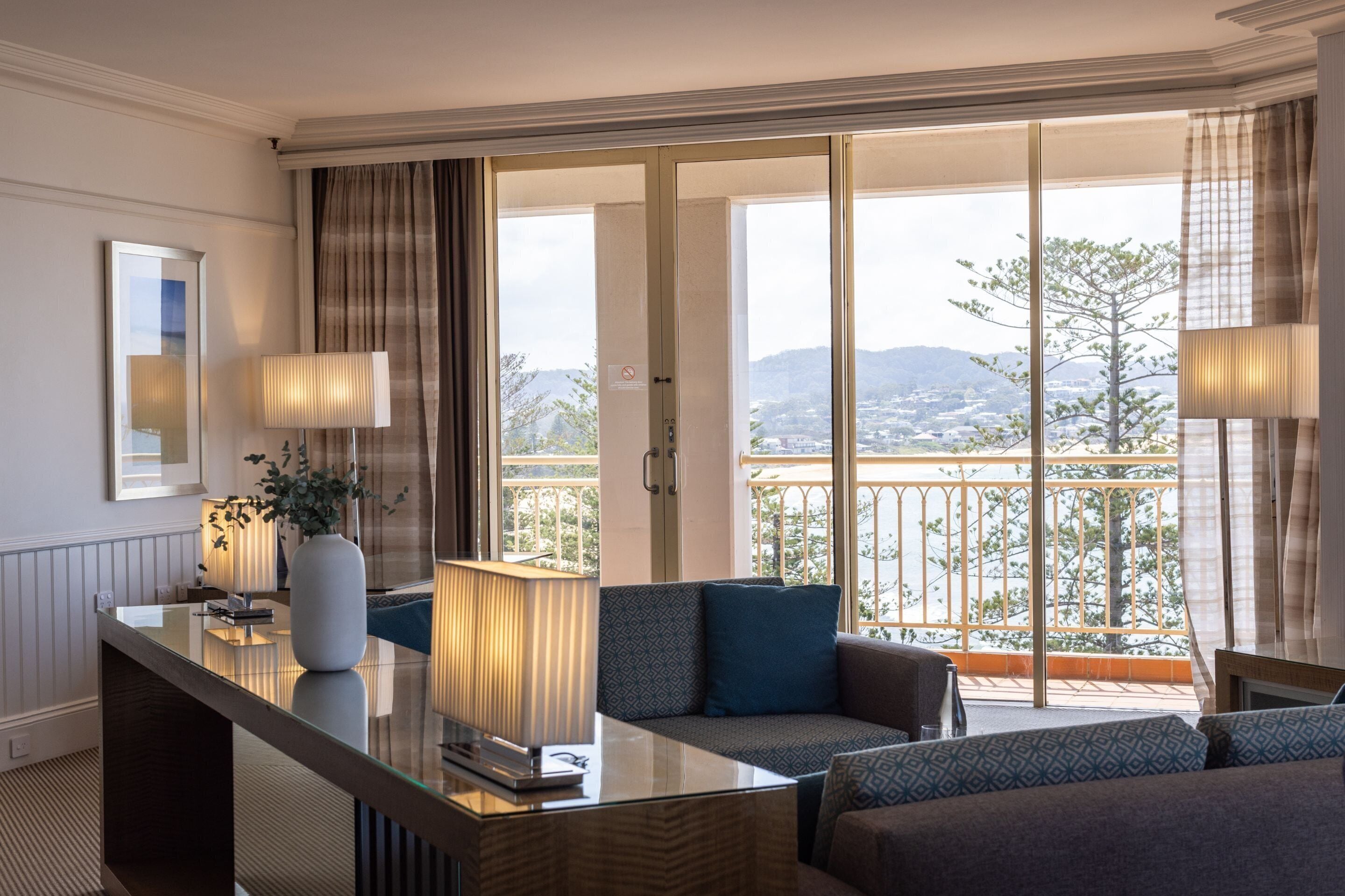 A modern hotel room with a balcony, a sofa, a coffee table, and a lamp.