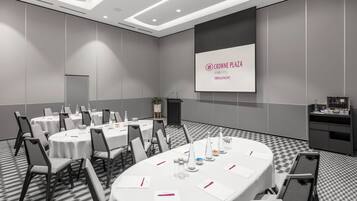 Un salón de conferencias con mesas redondas, sillas y una pantalla de presentación que muestra 'CROWNE PLAZA AN IHG HOTEL TERRIGAL PACIFIC'.